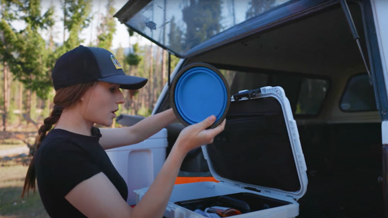 A woman holding up a blue travel water bowl from a first aid kit