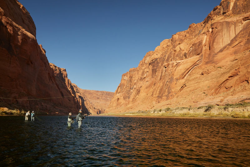A western river canyon with anglers wading in the distance.