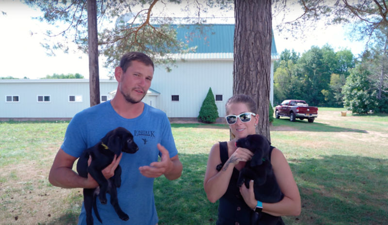 Ethan & Kat Pippitt both holding black lab puppies.
