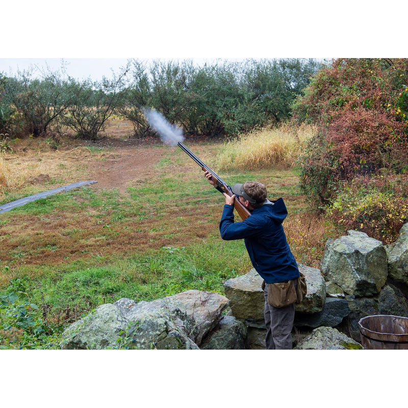 A man standing behind a rock wall shooting a shotgun