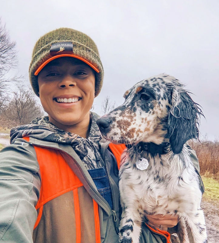 Melinda Benbow dressed in blaze orange holds a speckled hunting dog.