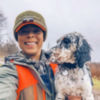 Melinda Benbow dressed in blaze orange holds a speckled hunting dog
