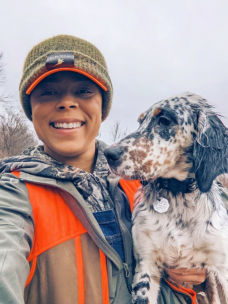 Melinda wearing a hat and camo holding her black and white dog