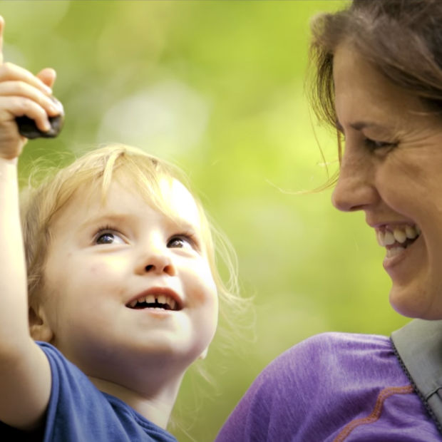 A smiling mother holds a small child who is pointing upwards.