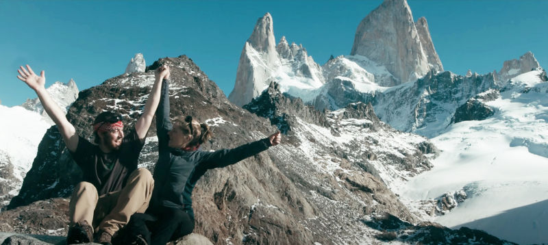 A mother and son with arms raised in celebration on top of a mountain.