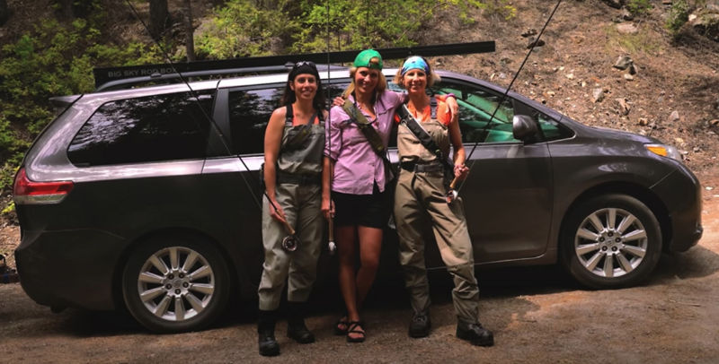 Three women in fishing gear standing in front of a car.