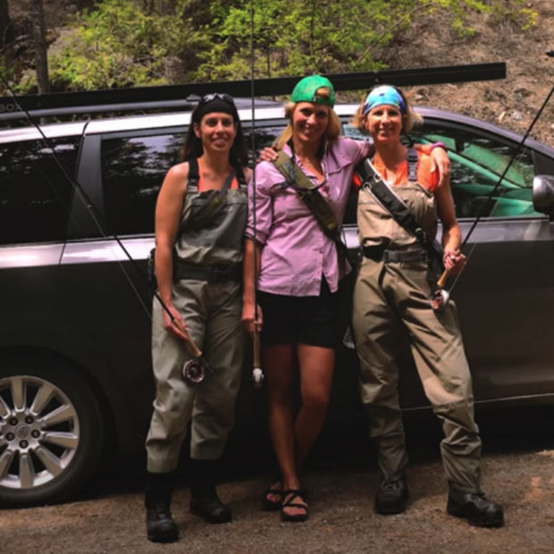 Three women in fishing gear standing in front of a car.