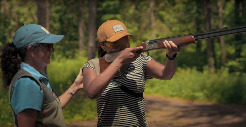 A shooting instructor guides a student into a correct position.