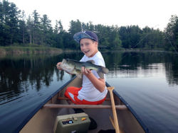 A child celebrates holding largemouth bass in canoe