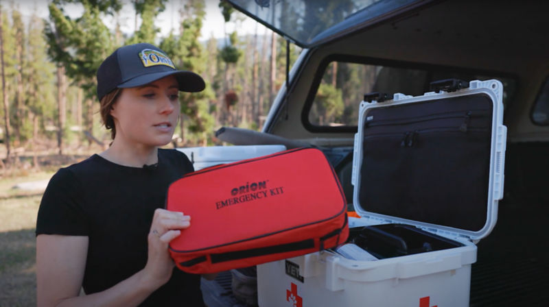 A woman holding a red first aid box at the back of a truck