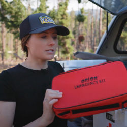 Madeline holding a dog first aid kit standing by the trunk of a car