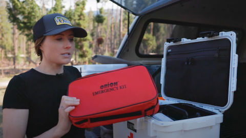 A woman holding a red first aid box at the back of a truck