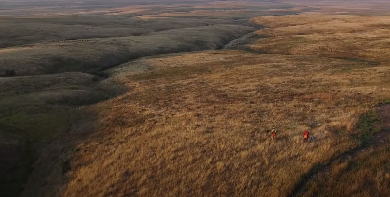 A drone view of two hunters in a vast grassland of rolling hills.