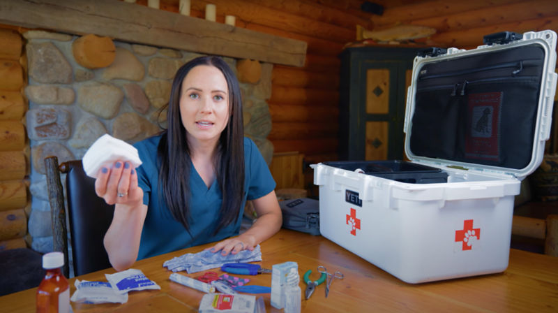 A woman wearing a blue shirt with long black hair sitting at a table going through a first aid kit